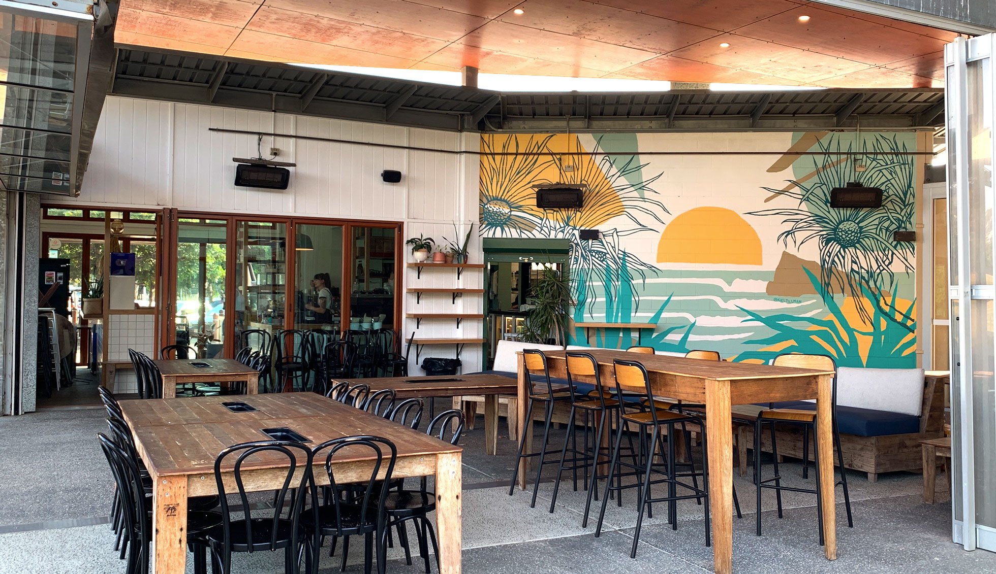 The mural features pandanus trees, a surfbreak and a sunrise in blues, aquas and yellow