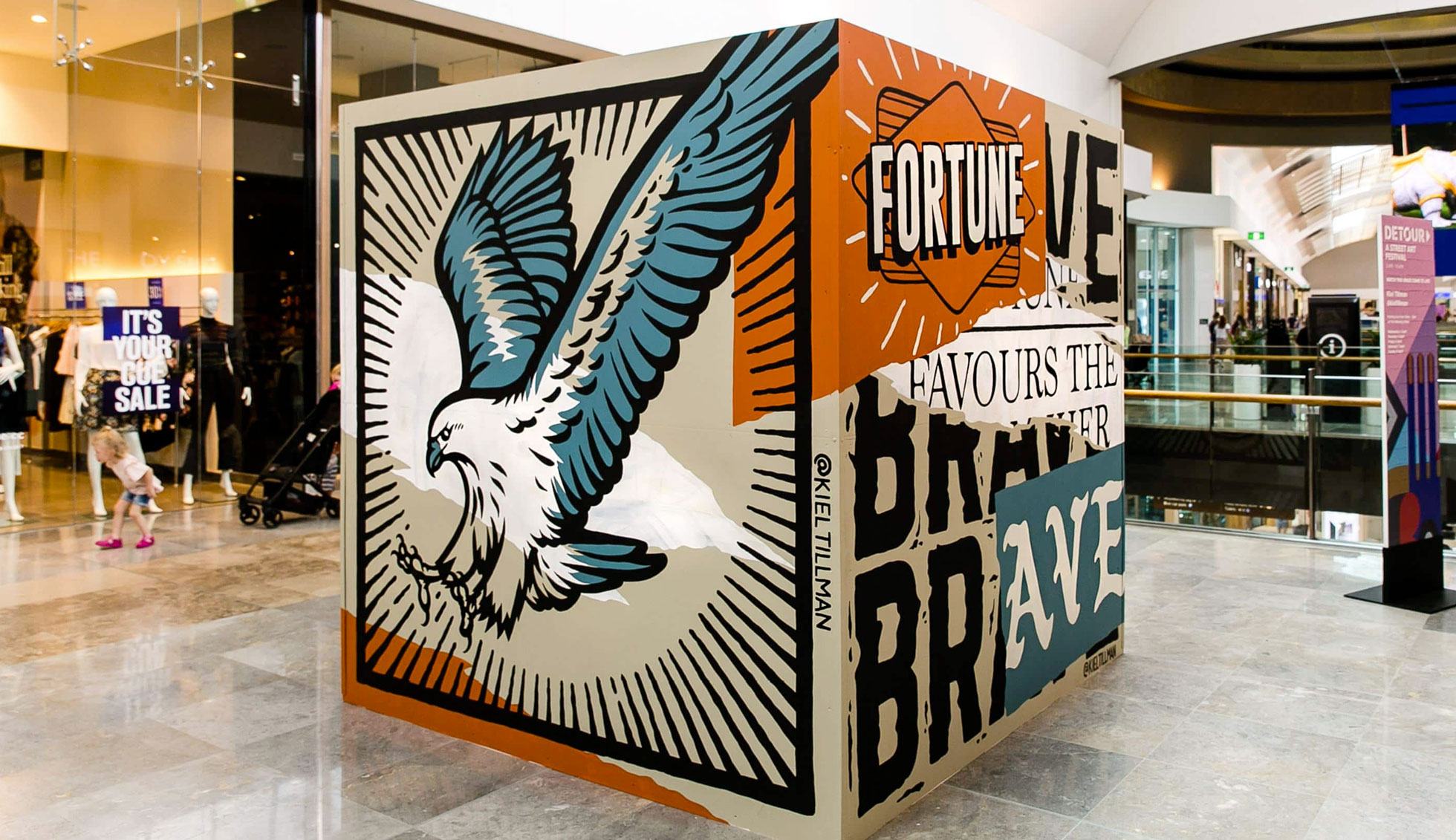 A freestanding cube is covered in an iconic Tillman mural, placed in the centre of the shopping walkway