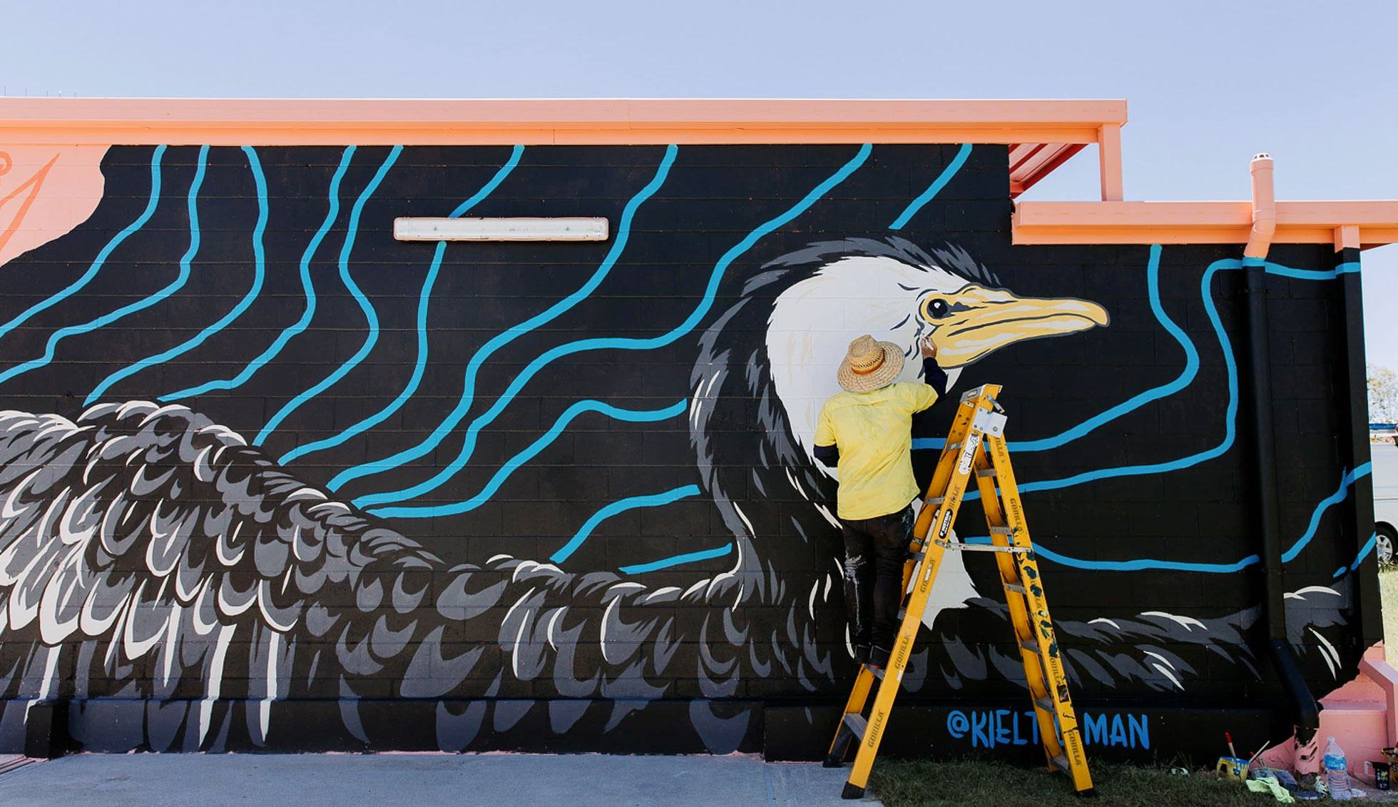 Local mural artist Kiel Tillman paints a giant bird onto the side of a water building for Gold Coast council