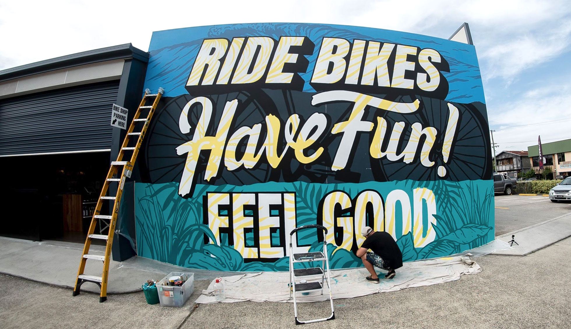 Mural artist Kiel Tillman squats down low to finish the final stages of the Trek mural
